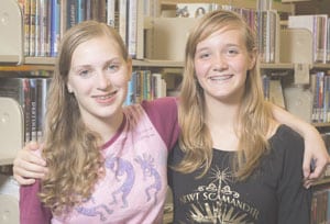Teenage girls smiling in front of a book shelf at the library