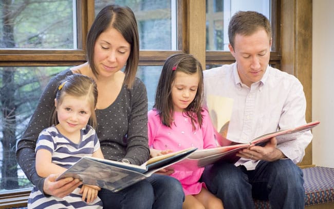 A family of a mother, father, and two young daughters reading children's books