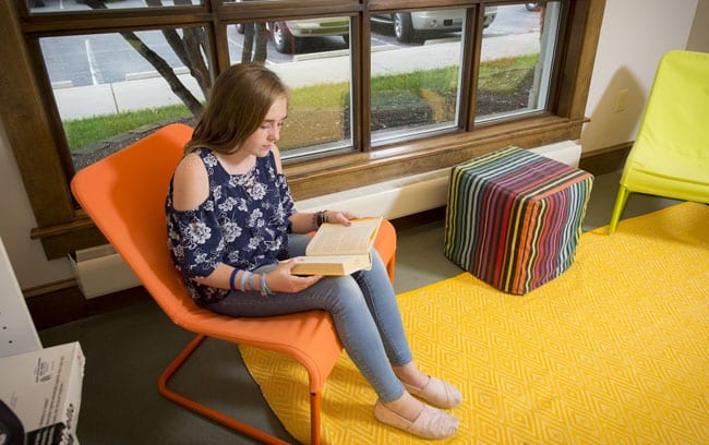 Teen girl sitting by the window reading a book