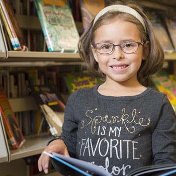 A young girl smiling in front of a shelf of kids books