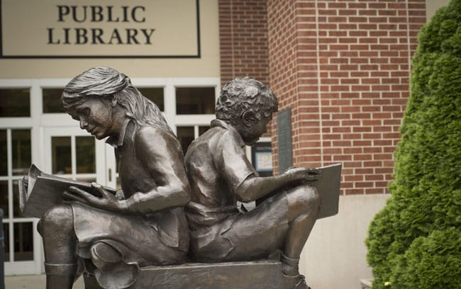 The statue of a young boy and girl sitting back to back reading