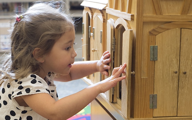 Young child playing at the library with a wooden barn toy