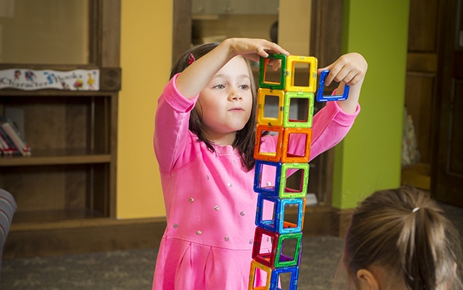 Little girl in a pink shirt building a tower with blocks