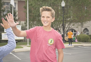 Young teen with blond hair and a red shirt giving a highfive