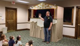 Man standing in front of puppet stage talking with children