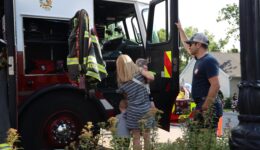 Caregiver and children climbing in the cab of fire truck while fire fighter looks on