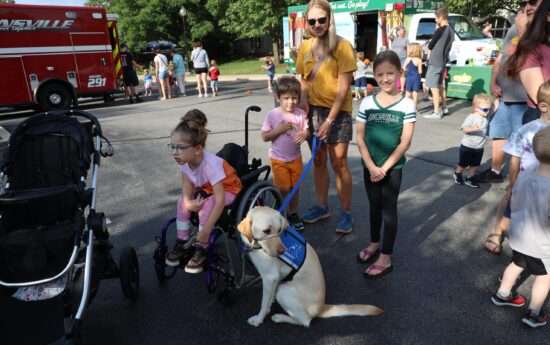Caregiver and children waiting in line, one child in wheelchair holding leash of service dog