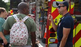 Firefighter standing beside fire truck talking to man with backpack