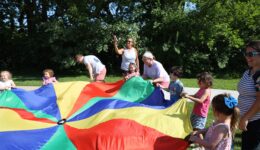 Librarians, children and caregivers playing with a parachute at the park