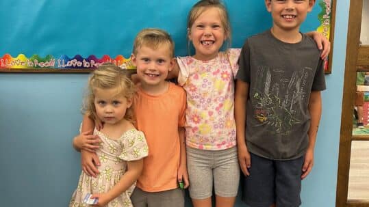 four siblings in front of bulletin board