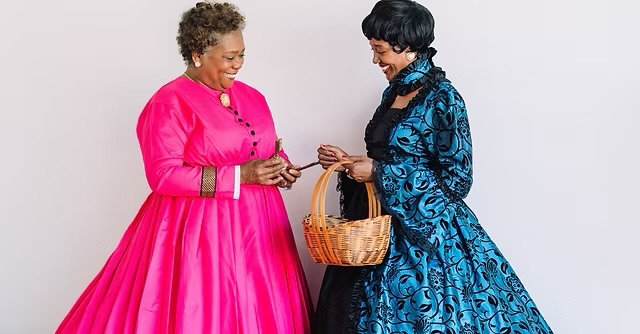 Two women in gowns face each other smiling and holding a basket.