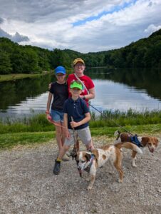 One adult, two kids, and 2 dogs in front of a lake.